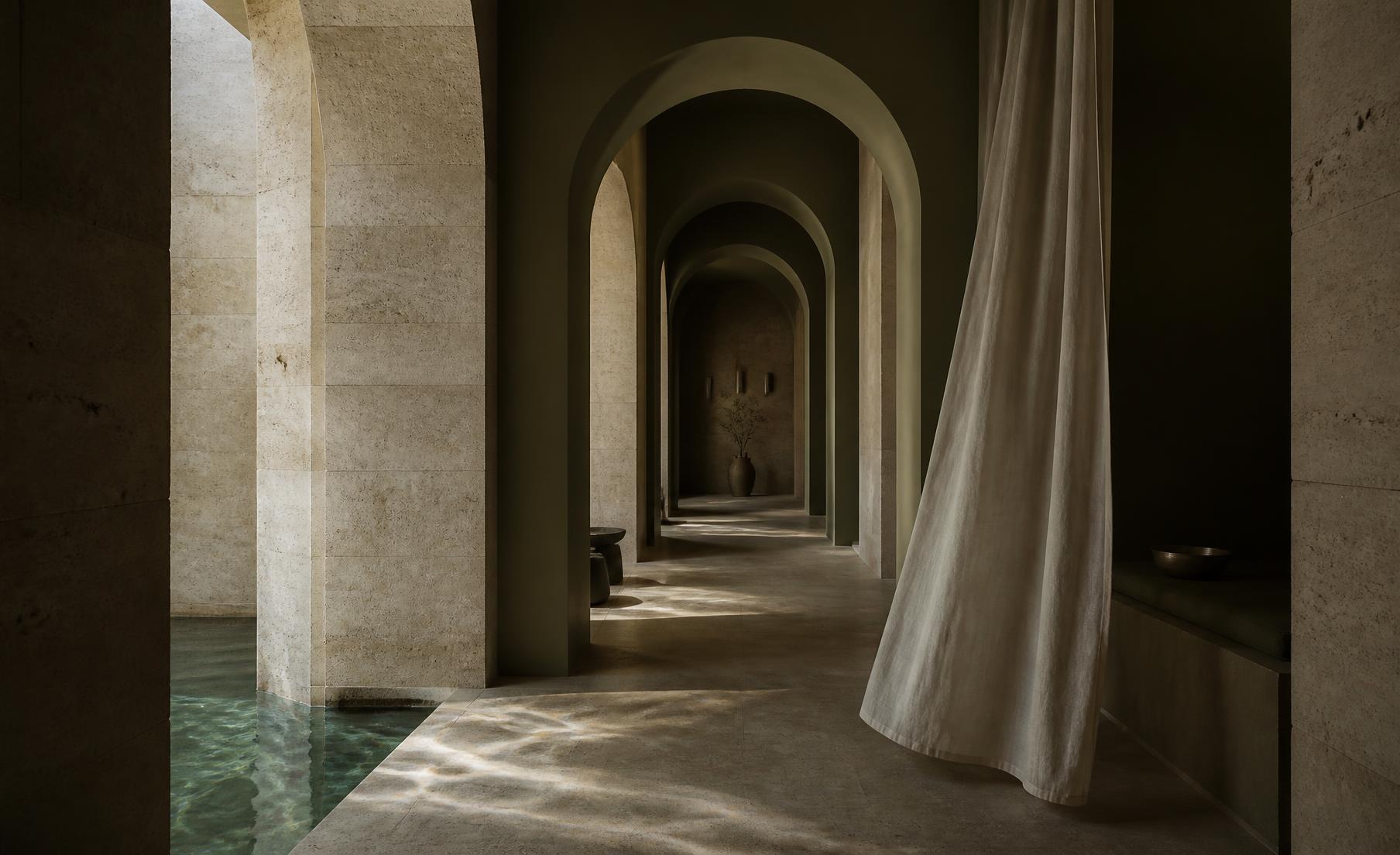 Arched limestone spa corridor with reflected water light